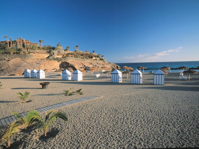 Arena, pasarela y casetas junto al mar en Playa del Duque
