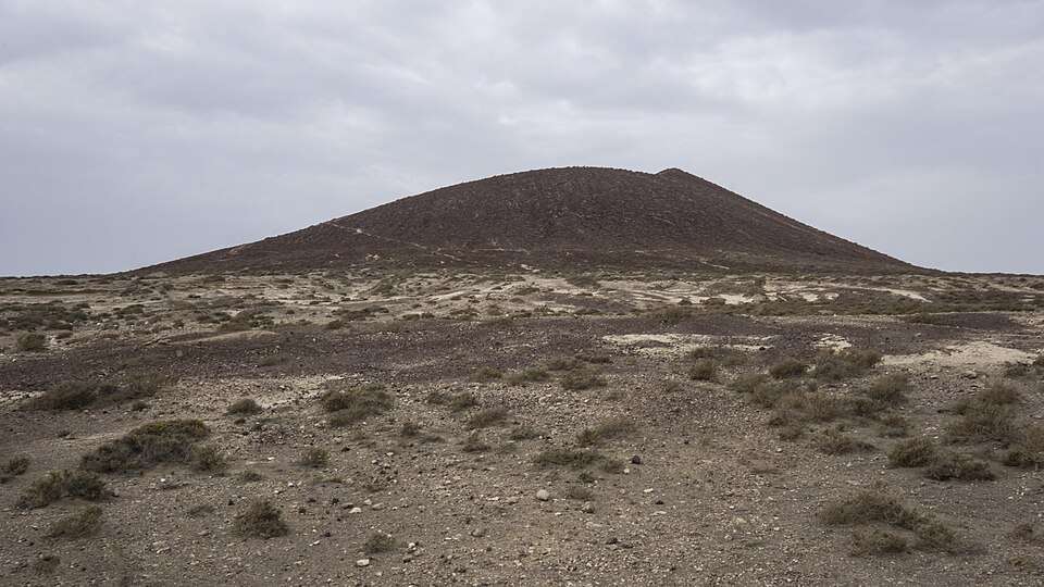 Cono volcánico de Montaña Roja sobre un paisaje de arena, roca y vegetación baja